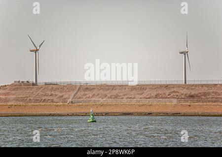 due turbine eoliche in piedi su una diga circondata da recinzioni Foto Stock