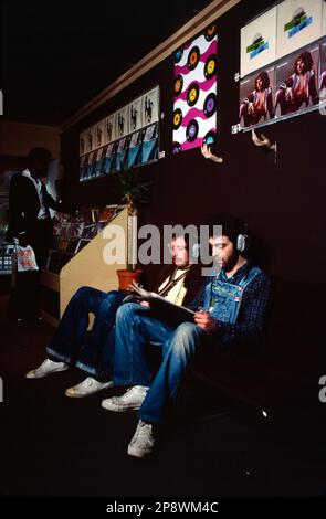 Regno Unito, Londra. 1977. Ascolto di dischi in vinile su cuffie in un negozio di dischi. Le ultime copertine sul muro tra cui Fleetwood Mac - Rumours, Peter Gabriel - il suo primo album solista e Peter Frampton - i'm in You. Foto Stock