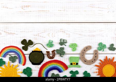 Concetto del giorno di San Patrizio. Composizione a maglia di un cappello verde, un ferro di cavallo, un sole, un arcobaleno e shamrock verde su uno sfondo di legno bianco. Centro di copiatura Foto Stock