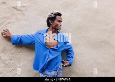 Vista laterale di un giovane ragazzo in una camicia blu appoggiata su un muro e guardando lontano Foto Stock