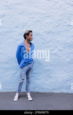 Tutta la lunghezza di un ragazzo in una camicia blu in piedi alla parete e guardando lontano Foto Stock