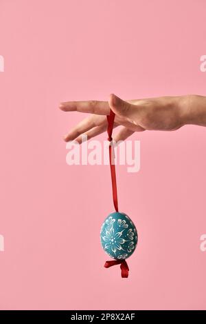 Mano del bambino che tiene un uovo di Pasqua blu decorato con cera davanti a sfondo rosa Foto Stock