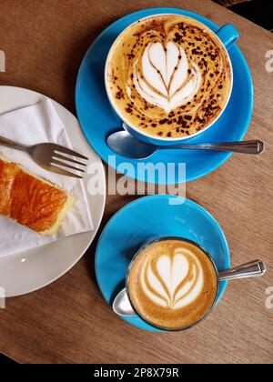 Vista dall'alto di tazze di caffè decorate (arte del caffè) e fetta di torta al limone Foto Stock