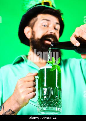 San Patrizio. Uomo felice che versa birra verde in vetro. Leprechaun beared in cappello verde con trifoglio in bicchiere di birra. Focalizzazione selettiva sulla tazza di Foto Stock