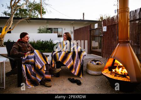Una coppia si siede fuori al crepuscolo e si gode un fuoco nella chiminea nel cortile di un motel sulla strada nel deserto alto. Foto Stock