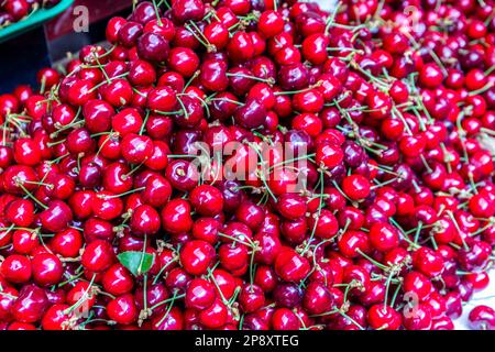 Abbondanza di ciliegie rosse con gambi, raccolte, nella bancarella del mercato centrale di Kutaisi (Bazaar Verde, Mtsvane Bazari). Foto Stock