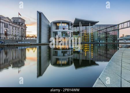 Quartiere governativo di Berlino con il fiume Sprea in serata. Reichstag e Paul Löbe Casa con riflessione sulla superficie dell'acqua al tramonto. Foto Stock