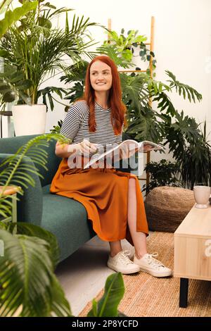 Bella donna che legge rivista sul divano in camera Foto Stock