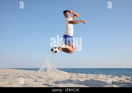 Uomo che gioca a calcio sulla spiaggia vicino al mare Foto Stock