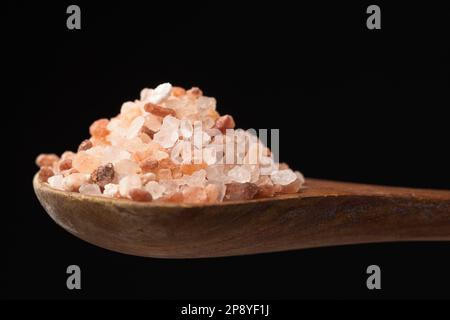 Una foto ravvicinata del sale marino himalayano grossolano su un cucchiaio di legno su sfondo nero. Foto Stock