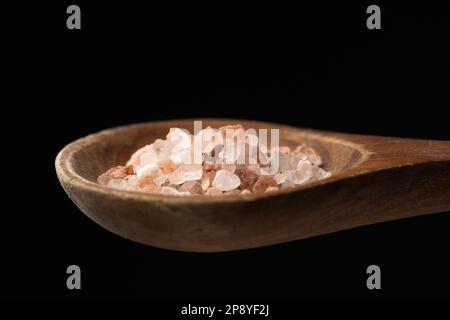 Una foto ravvicinata del sale marino himalayano grossolano su un cucchiaio di legno su sfondo nero. Foto Stock