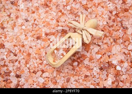 Una foto di studio a forma di piatto di una piccola paletta di legno riempita con sale grossolano sulla cima di un mucchio di sale marino himalayano rosa. Foto Stock