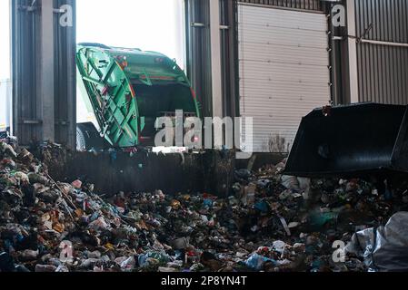 Un autocarro per rifiuti scarica i rifiuti domestici nella camera di ricezione di un impianto di smistamento rifiuti Foto Stock