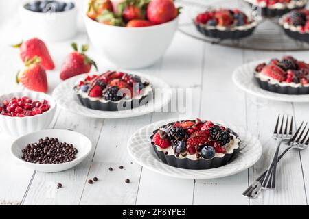 Crostate di cheesecake a base di frutti di bosco individuali fatte in casa su un tavolo di legno bianco. Foto Stock