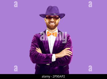 Ritratto di felice uomo portatore con cappello viola, tuta, cravatta d'arco pazzo e occhiali da festa Foto Stock