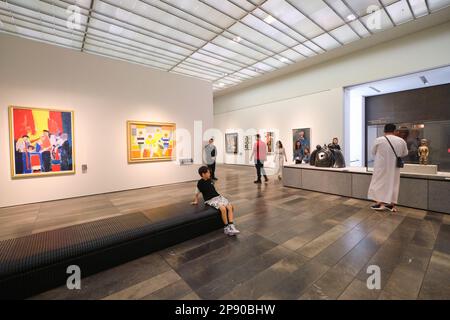 Un ragazzo riposa su una panchina in una sala galleria che espone arte moderna e astratta Al museo d'arte del Louvre francese ad Abu Dhabi, Emirati Arabi Uniti. Foto Stock