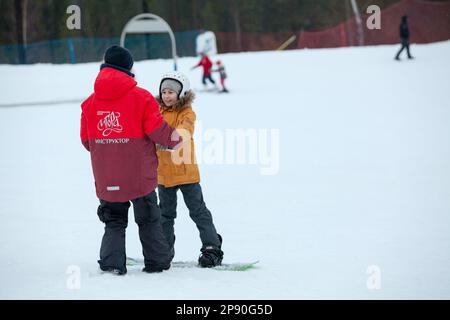 St Pietroburgo, Russia-circa gennaio, 2018: L'istruttore tiene le mani del bambino mentre scivola lungo la pista su uno snowboard. Allenamento di snowboard Foto Stock