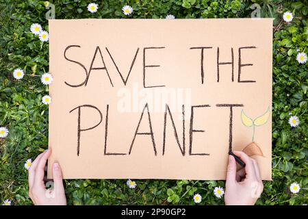 Attivista che scrive il poster "SAVE THE PLANET" per la manifestazione contro il riscaldamento globale e l'inquinamento della terra. Banner di cartone per protestare contro il cambiamento climatico. Foto Stock