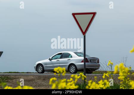 Il segnale lascia il posto al conducente quando si esce dall'autostrada a un incrocio rurale sullo sfondo di un auto di passaggio. Foto Stock