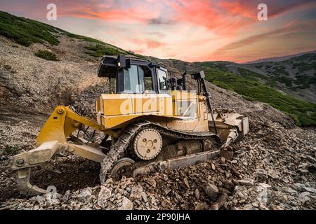 Escavatore giallo su un nuovo cantiere, con il sole luminoso e il bel cielo rosso sullo sfondo Foto Stock