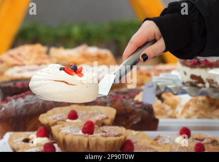 Primo piano di un venditore presso un negozio di pasticceria che raccoglie un dessert Pavlova al mercato alimentare di strada degli agricoltori di Praga nel freddo giorno di primavera. Nessuna intelligenza artificiale. Foto Stock