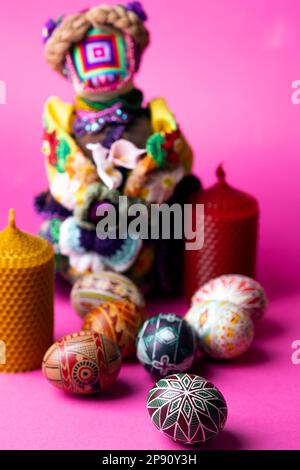 buona pasqua. Bellissimo uovo di Pasqua Pysanka fatto a mano, bambola e candele Motanka su sfondo rosa Foto Stock