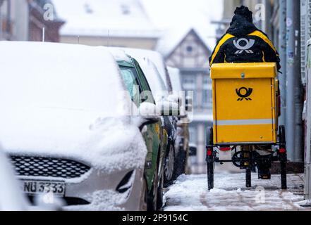 Schwerin, Germania. 10th Mar, 2023. Un portaritone sta guidando la sua bicicletta in una nevicata pesante nella città vecchia. Il 10 marzo 2023 inizia il 4th° turno di negoziati nella controversia sulla contrattazione collettiva di Deutsche Post. Si tratta di un nuovo contratto collettivo per circa 160.000 dipendenti della divisione Post & Paket Deutschland Group. Verdi sta chiedendo un aumento di paga di 15 per cento. Credit: Jens Büttner/dpa/Alamy Live News Foto Stock