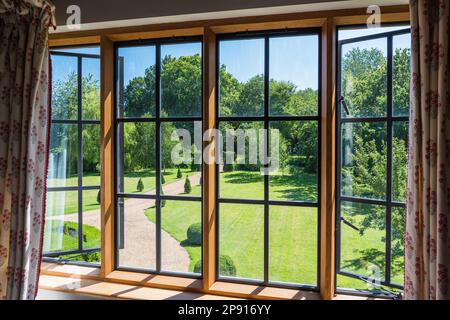 Vista attraverso la moderna finestra di vetro con piombo fino al giardino della residenza elisabettiana di grado II, Suffolk, Regno Unito Foto Stock