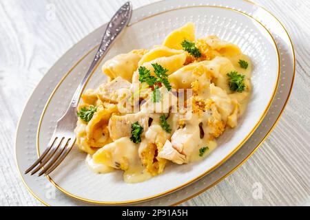 primo piano di pollo cremoso e cremoso e pasta conchiglie cuocere in ciotola bianca con forchetta su tavolo bianco, vista orizzontale dall'alto Foto Stock