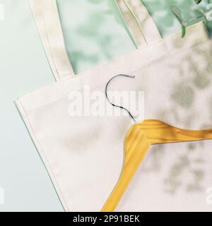 Concetto di shopping, acquisto o vendita sostenibile. Eco-friendly primavera ancora vita con appendiabiti in legno su borsa shopping in tessuto bianco su sfondo blu con Foto Stock