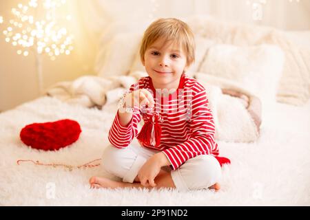 Carino ragazzo prescolare, giocando con bracciali bianchi e rossi. Martenitsa, varietà di filati bianchi e rossi, tradizione folcloristica bulgara, primavera di benvenuto Foto Stock