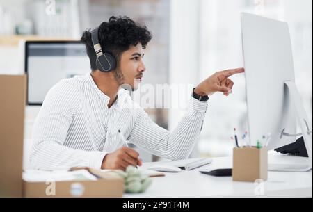 Meglio leggere con attenzione questo. Scatto di un giovane uomo d'affari che indossa le cuffie mentre lavora su un computer in ufficio. Foto Stock
