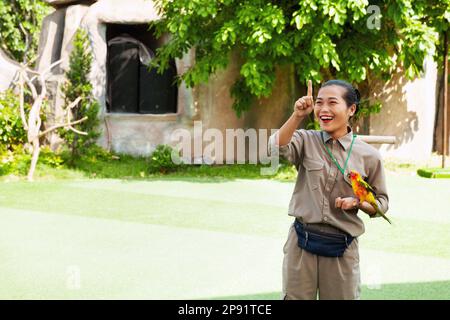 Nha Trang, Vietnam - 4 aprile 2018: Spettacolo di uccelli in un parco divertimenti. Bird trainer con paracadute Sun. Giovane donna asiatica che tiene un pappagallo colorato Foto Stock