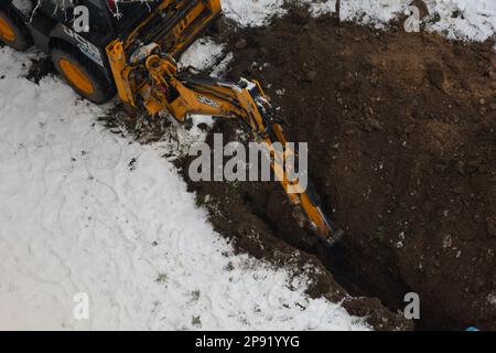 Tiraspol, Moldova - 31 gennaio 2023: L'escavatore JCB scava una trincea per la posa di un tubo fognario in una nuvolosa giornata invernale. Messa a fuoco selettiva, profondità di fi ridotta Foto Stock