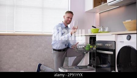 Giovane uomo che prende bicchiere da lavastoviglie in cucina Foto Stock