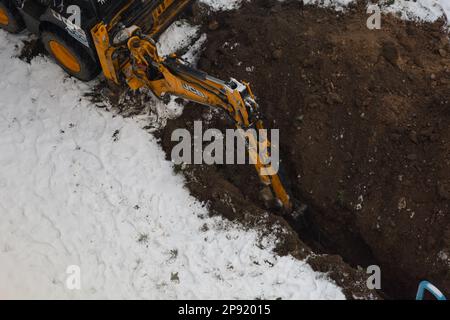 Tiraspol, Moldova - 31 gennaio 2023: L'escavatore JCB scava una trincea per la posa di un tubo fognario in una nuvolosa giornata invernale. Messa a fuoco selettiva, profondità di fi ridotta Foto Stock