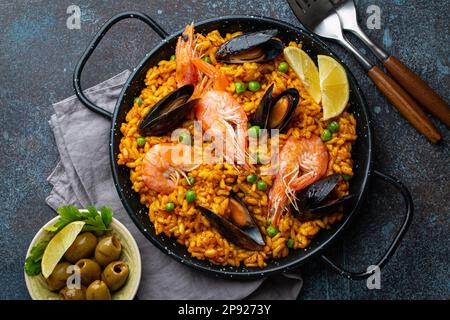 Piatto classico della Spagna, paella di pesce in padella tradizionale su sfondo rustico blu cemento vista dall'alto. Paella spagnola con gamberetti, pinze, cozze Foto Stock