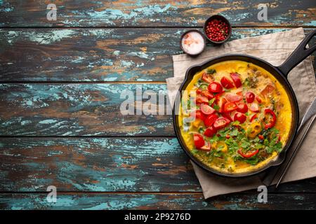 Frittata sana in padella di ghisa con uova sbattute fritte e verdure di stagione su sfondo rustico in legno. Frittata italiana con spinaci biologici Foto Stock