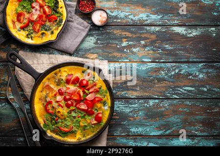 Frittata sana in due padelle di ghisa con uova sbattute fritte e verdure di stagione su sfondo rustico in legno. Omelette italiana con biologico Foto Stock