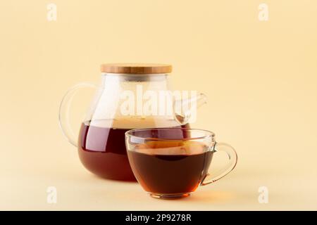 Tè nero biologico appena preparato in teiera trasparente in vetro e teacup trasparente in vetro su sfondo beige, fuoco selettivo Foto Stock