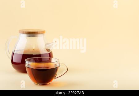 Tè nero biologico appena preparato in teiera trasparente in vetro e teacup trasparente in vetro su sfondo beige, fuoco selettivo. Tè con spazio per il testo Foto Stock