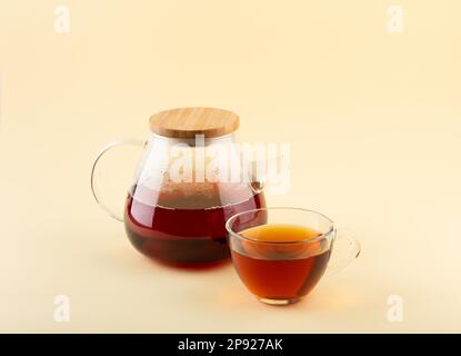 Tè nero biologico appena preparato in teiera trasparente in vetro e teacup trasparente in vetro su sfondo beige, fuoco selettivo Foto Stock