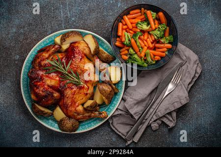 Delizioso pollo intero arrosto con pelle dorata croccante e verdure al vapore in ciotola vista dall'alto piatto adagiato su rustico piano da tavolo in cemento Foto Stock