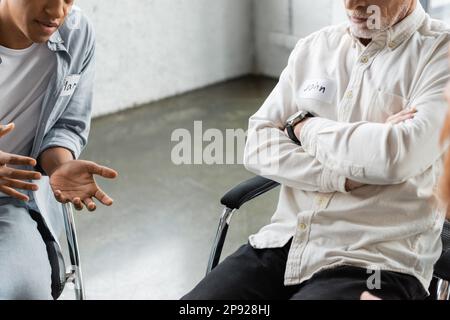 Vista ritagliata della persona afroamericana che parla con l'uomo durante la riunione alcolisti nel centro di riabilitazione, immagine stock Foto Stock