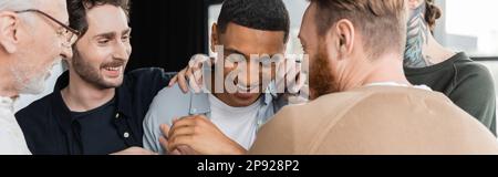 Allegro gruppo abbracciando l'uomo afroamericano durante anonimi alcolisti incontro nel centro di riabilitazione, banner, immagine stock Foto Stock