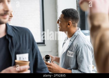 Sorridente afroamericano che versa la bevanda dai thermos e che parla durante la riunione degli alcolisti nel centro di riabilitazione, immagine di scorta Foto Stock