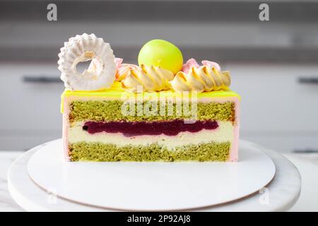 Fetta di torta al pistacchio con crema e ripieno di fragole, decorata con cioccolato, meringhe, caramelle Foto Stock