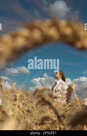 Pregate per l'Ucraina. Ragazza Ucraina in un campo di grano. Una ragazza in un campo di grano prega per la pace in Ucraina. Donna felice che celebra il giorno dell'Indipendenza Foto Stock