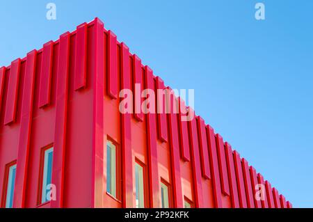 Moderno edificio di uffici dall'architettura rossa. Lamiere che coprono l'esterno della struttura. Edificio di stile futuristico unico. Cielo chiaro sul retro Foto Stock