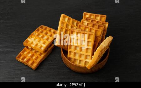 Waffle belgi isolati, biscotti quadrati in legno, cialde d'oro fatte in casa, cialde biscottate su sfondo nero Foto Stock